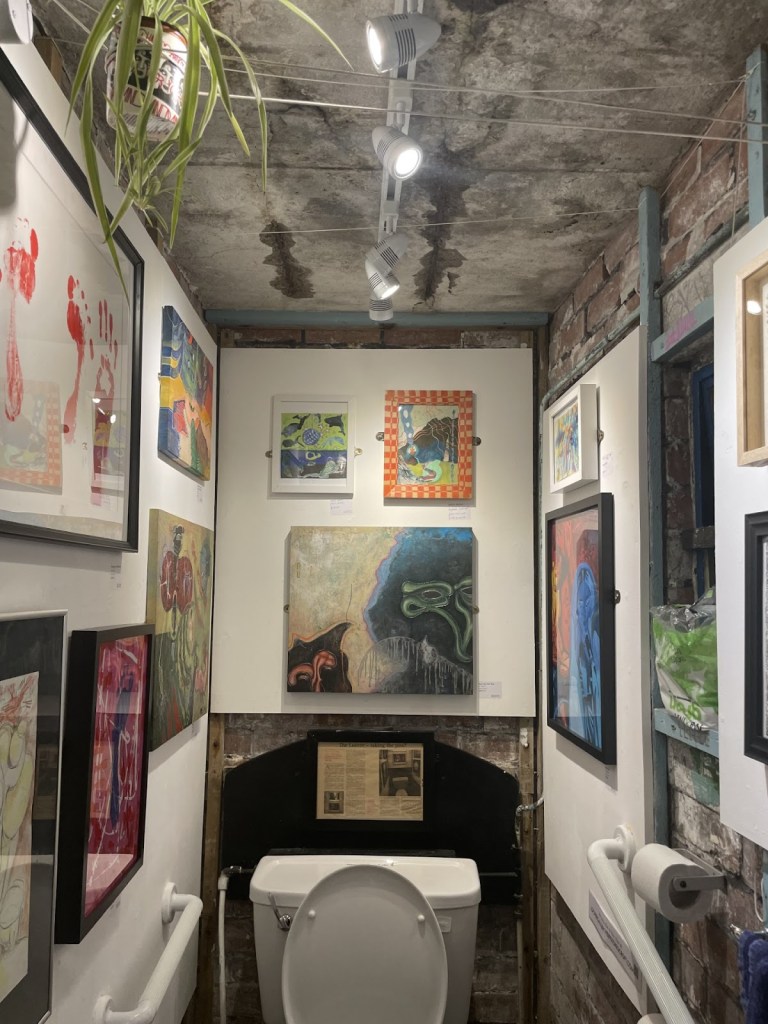 A bathroom stall with walls covered in framed artwork